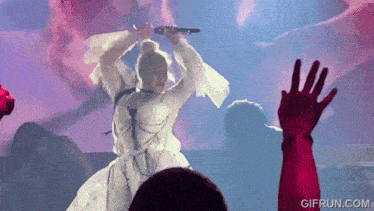 a woman in a white dress is singing into a microphone with a gifrun.com watermark