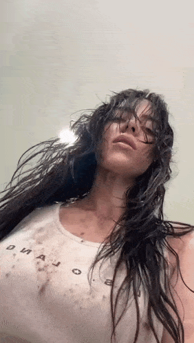 a woman with long dark hair is wearing a white tank top and has wet hair .