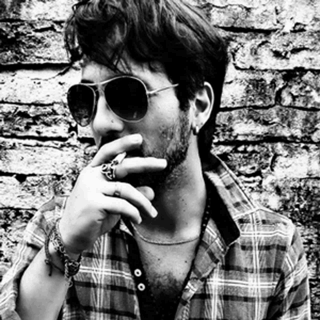 a man wearing sunglasses and a plaid shirt is covering his mouth with his hand