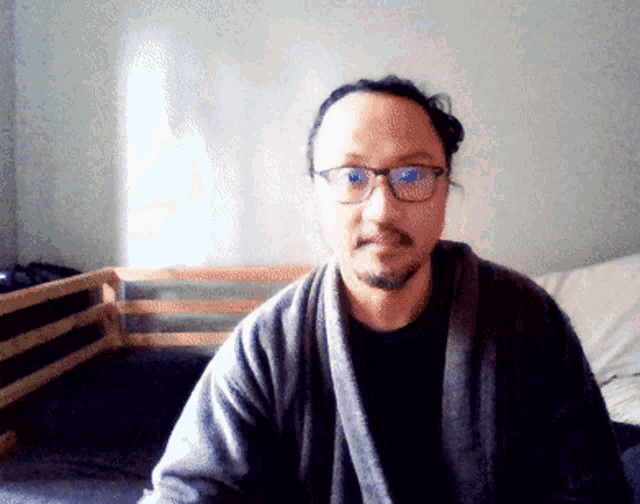 a man wearing glasses and a robe is sitting in front of a bed