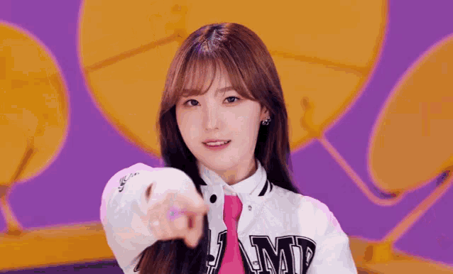 a girl wearing a white jacket and a pink tie points at the camera .