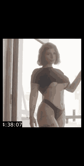 a woman in a black top and black panties is standing in front of a window with a timer .