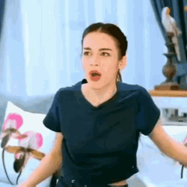a woman in a blue shirt is sitting on a bed with her mouth open and a microphone in her mouth .