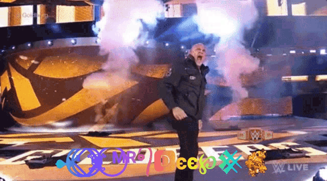 a man in a black jacket stands on a stage with smoke coming out of his mouth in front of a w live sign