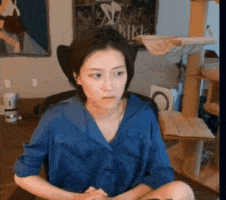 a woman wearing a blue shirt is sitting in front of a cat tree