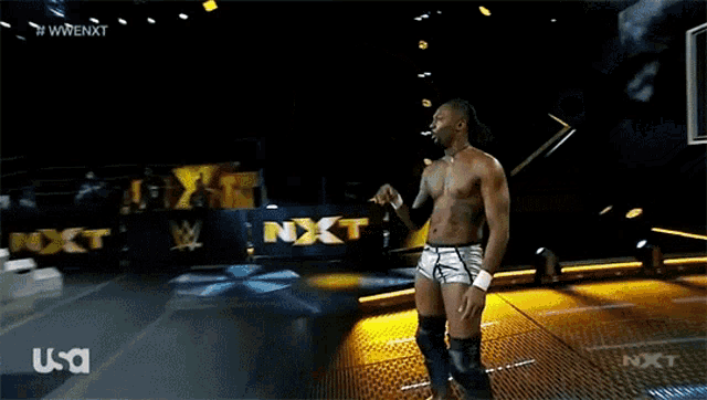 a wrestler stands in front of a sign that says nxt on it