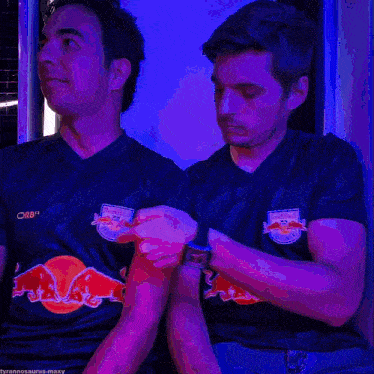 two men wearing blue red bull shirts are looking at their watches
