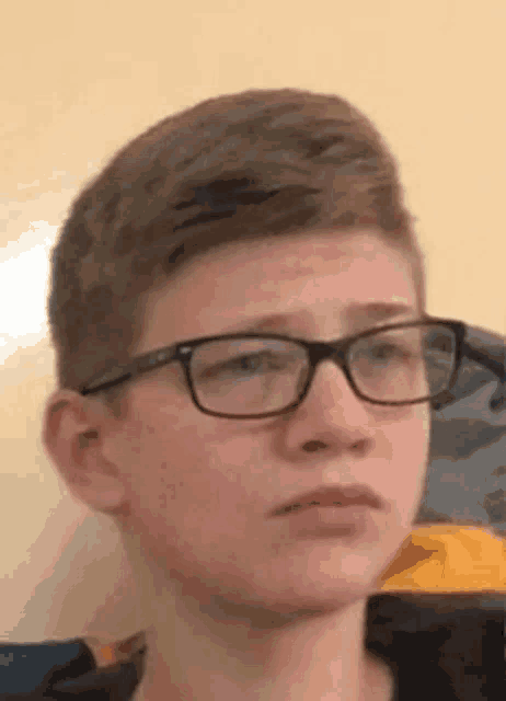 a young boy wearing glasses is looking at the camera with a sad look on his face .