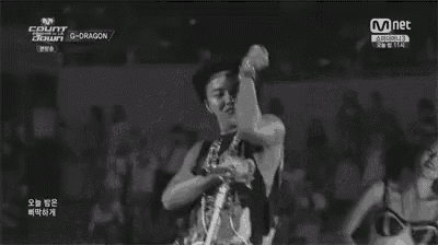 a black and white photo of a man singing into a microphone while dancing in front of a crowd .