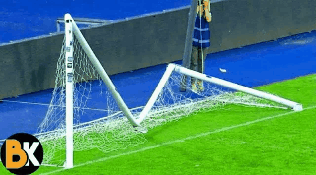 a broken soccer goal on a field with the letter bk in the corner