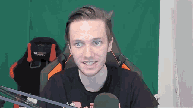 a man is sitting in front of a green screen with a microphone in front of him .