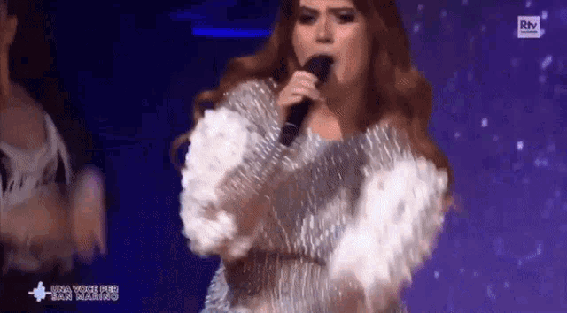 a woman singing into a microphone on a stage with a rtv logo in the background