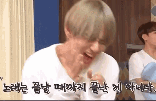 a man with blonde hair is making a funny face and laughing while another man looks on .