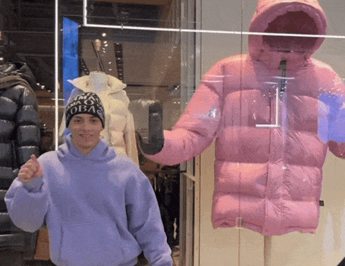 a man in a purple hoodie stands in front of a mannequin wearing a pink jacket with a hood