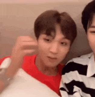 two young men are sitting next to each other on a couch and one of them is holding a pillow .