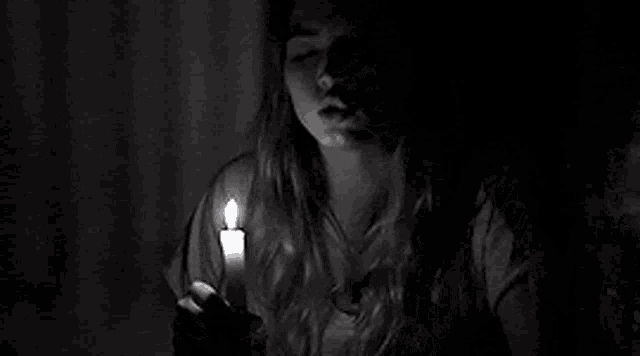 a black and white photo of a woman holding a lit candle .