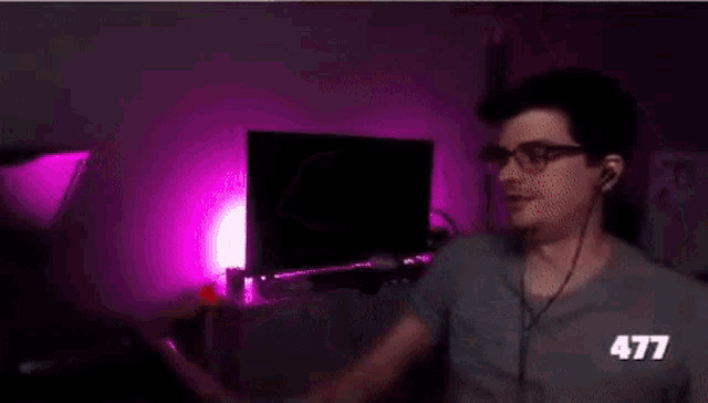 a man in a gray shirt is sitting in front of a purple light in a dark room .