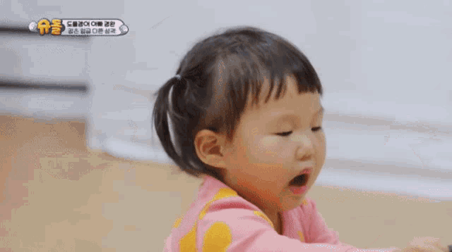 a little girl in a pink and yellow polka dot shirt is making a fist