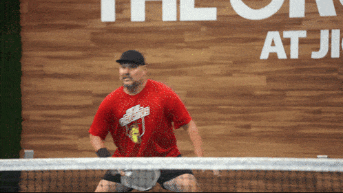 a man in a red shirt is playing tennis in front of a sign that says " the on "