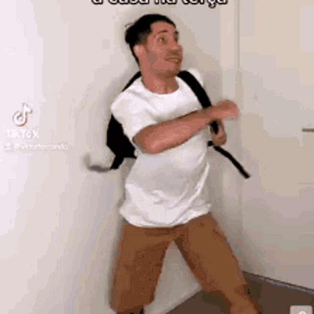 a man wearing a white shirt and brown shorts is standing in a corner .