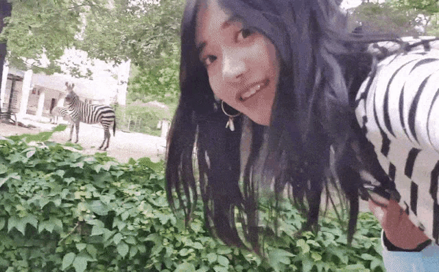 a woman in a black and white striped shirt stands in front of a zebra