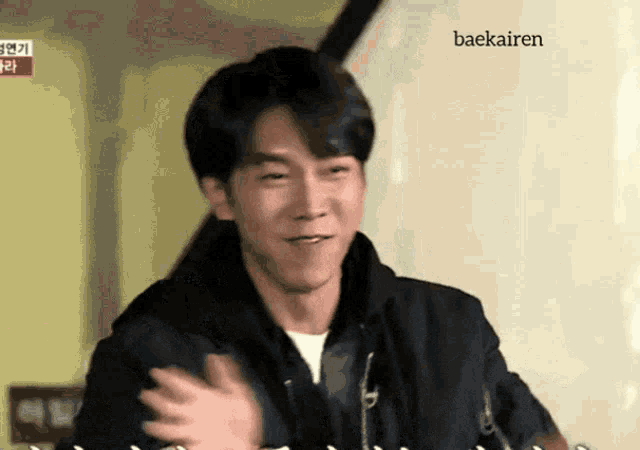 a man in a black jacket waves his hand in front of a sign that says baekairen