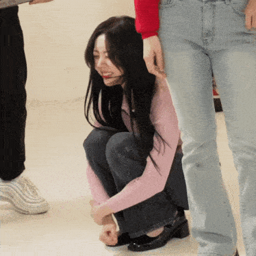 a woman in a pink sweater is kneeling on the floor