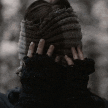 a person wearing a knitted hat and gloves is covering their ears with their hands .