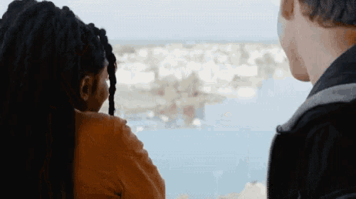 a man and a woman are looking out a window at a body of water