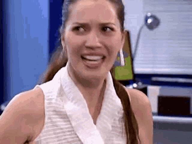 a woman is making a funny face while wearing a white tank top and earrings .