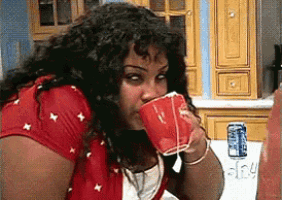 a woman in a red shirt drinking from a red cup next to a can of soda