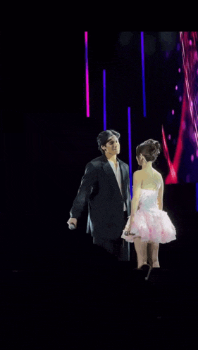 a man in a suit is standing next to a woman in a pink dress on a stage .