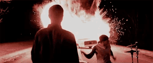 a man and a woman are standing in front of an explosion in a car .