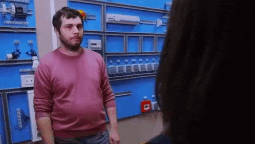a man in a pink sweater is standing next to a woman in a room with a blue wall .