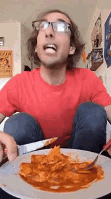 a man in a red shirt is eating a plate of food