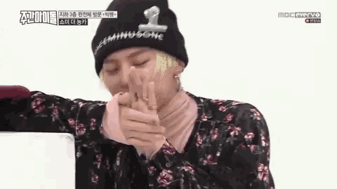 a man wearing a black beanie and a pink sweater is covering his face with his hands .