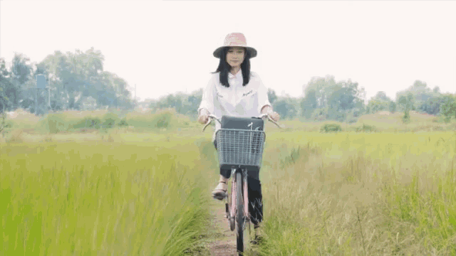 a woman wearing a white shirt and a pink hat is riding a bicycle through a grassy field