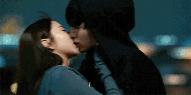 a man and a woman are kissing in front of a city skyline at night .