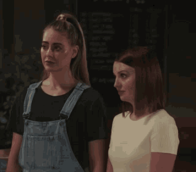 two women are standing next to each other and one of them is wearing overalls