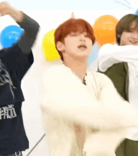 a man with red hair is dancing in front of balloons while another man looks on .