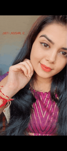a close up of a woman 's face with a purple and gold top and a red bracelet