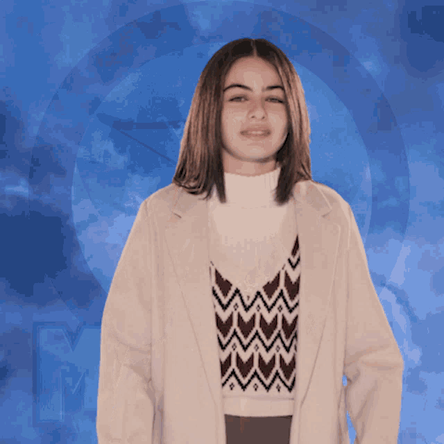 a woman stands in front of a blue background with the letter m in the corner