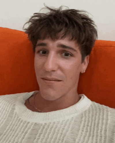 a young man wearing a white sweater is laying on an orange pillow