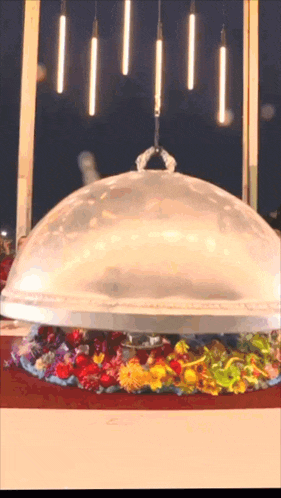 a clear dome with flowers underneath it is being lifted by a crane