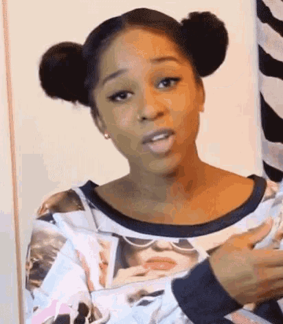 a woman with two buns in her hair is making a funny face while wearing a sweatshirt .