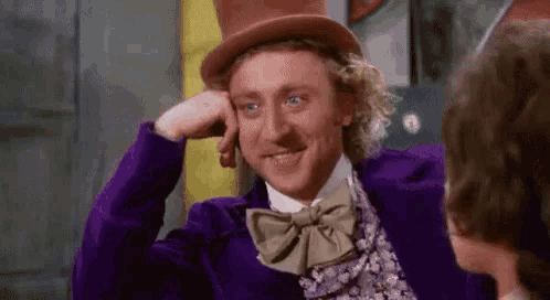 a man in a top hat and bow tie is smiling while holding his hand to his chin .