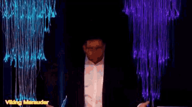 a man in a suit and white shirt is standing on a stage in front of purple lights .