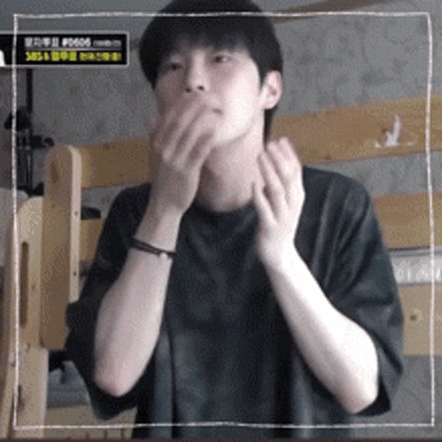 a young man covering his mouth with his hands in front of a sign that says # 0605 on it