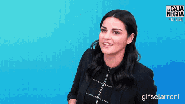 a woman is smiling in front of a blue background with la caja negra written on it