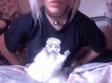 a woman in a black shirt is holding a white kitten .